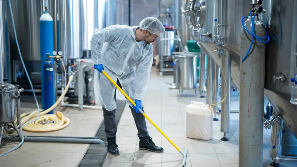 KCS-vakman tijdens industriële reiniging in een productieomgeving, volledig in hygiënische beschermkleding